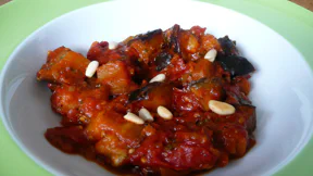 Salat aus groben Auberginenstücken und Tomaten, bestreut mit leicht angerösteten Pinienkernen