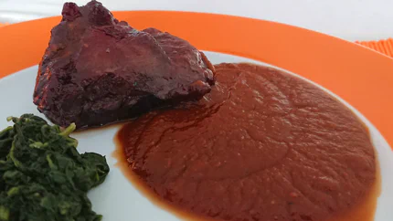 Ein Rinderbäckle liegt neben einer sämigen, braunen Sauce und Blattspinat auf einem Teller