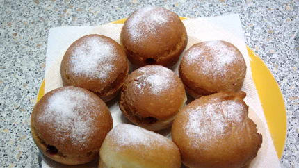 Sieben goldbraun frittierte Berliner liegen auf einem Teller, sie sind mit Marmelade gefüllt.