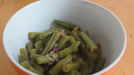 Eine Portion Bohnensalat aus grünen Bohnen, kleinen Zwiebelwürfeln, Essig und Öl.