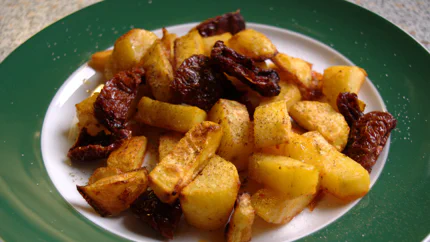 Goldbraune Bratkartoffeln mit leicht angebratenen, getrockneten Tomaten, garniert mit Salz und Pfeffer.