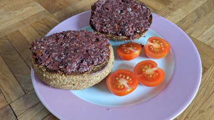 Zwei Brötchenhälften mit Bruschetta bestrichen liegen auf einem Teller. Daneben sind zwei halbierte Tomaten.
