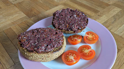 Zwei Brötchenhälften mit Bruschetta bestrichen liegen auf einem Teller. Daneben sind zwei halbierte Tomaten.
