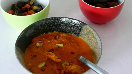 Eine Portion Butterhuhn aus groben Hühnerstücken, Tomaten-Joghurt-Sauce und Pistazien in einer Schale.