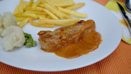 Ein Steak mit einer orangenen Sauce Café de Paris liegt neben Pommes und Blumenkohl auf einem Teller.
