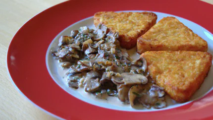 Eine sämige Sahnesauce mit feinen Champignonscheiben und Petersilie neben drei Rösti.