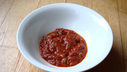 Sattrote Chipipaste mit Stücken von roten und grünen Chilischoten, Petersilie und Öl in einer Schale.