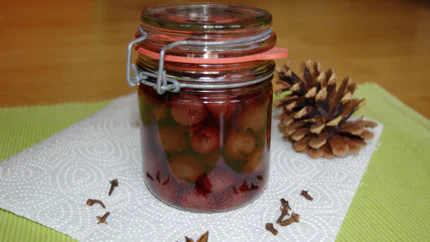 Ein Einmachglas mit entsteinten Kirschen in Kirschsaft und weihnachtlichen Gewürzen.