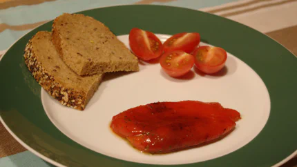 Eingelegte Paprika mit Pfeffer und Öl, daneben liegen Brotscheiben und Tomatenschnitze.