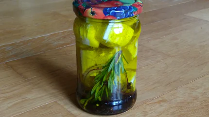 Ein Einmachglas mit großen Schafskäsewürfeln, Rosmarin, Zwiebelringen und Pfeffer in Öl.