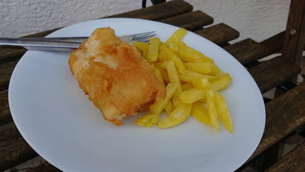 Ein Fischfilet in Backteigmantel liegt neben groben Pommes auf einem Teller.