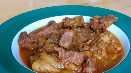 Grobe Rindfleischstücke und Lauchringe liegen in einer rotbraunen Sauce.