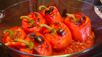 In einer Auflaufform stehen sechs gefüllte Paprika in einer Tomatensauce. Die Oberseiten der Paprika sind vom Grill gebräunt.