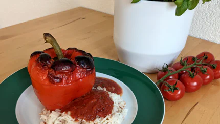 In einem tiefen Teller steht eine gefüllte Paprika auf einer Portion Reis mit Tomatensauce. Die Oberseite der Paprika is vom Grill gebräunt.