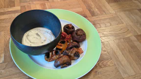 Braun gebackene und halbierte Champignons liegen auf einem Teller mit Joghurtdip mit Kräutern.