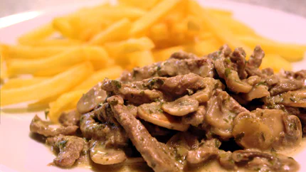 Kalbfleischstreifen und Champignonscheiben in einer Sahnesauce mit Petersilie neben goldgelben Pommes.