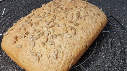 Ein hellbraun gebackenes Kastenbrot mit Sonnenblumenkernen liegt auf einem Rost.