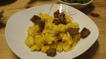 Spiralnudeln in Kartoffelbrei mit Croutons in einem tiefen Teller. Daneben steht ein Blattsalat.