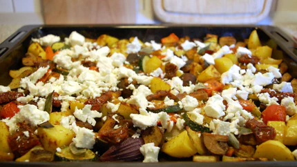 Viele gewürfelte Gemüsestücke liegen auf einem Backblech, darüber ist Feta verteilt. Schön bunt!