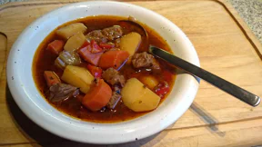 Rindfleisch-, Kartoffel- und Paprikawürfel liegen in einer roten Gulaschsuppe.