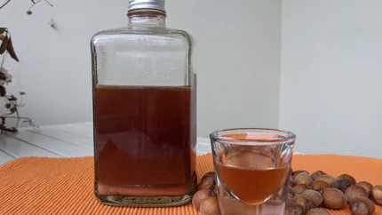 Haselnusslikör in einem Schnapsglas und einer eckigen Flasche umgeben von Haselnüssen.