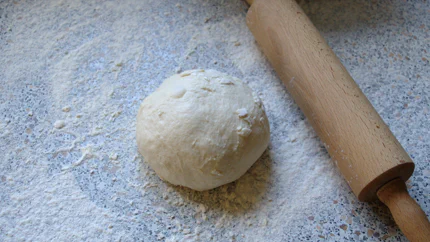 Eine Kugel roher Hefeteig mit Mehl neben einem Nudelholz.