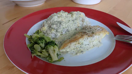 Ein ganzes Kabeljaufilet mit einer Sahnesauce mit Dill neben einer Portion Reis und Brokkoli.