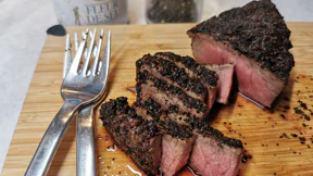 Ein Steak mit einem Mantel aus gemahlenem Kaffee liegt auf einem Brett. Es sind bereits Streifen abgeschnitten - das Innere ist nocht zartrosa.