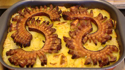 Vier gegrillte Streifen Bauchspeck liegen auf einer Schickt Kartoffeln, die auch braune Stellen haben.