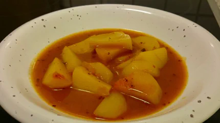 Grobe Kartoffelstücke schwimmen in einer Suppe mit Kräutern und Paprikapulver.