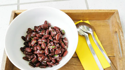 Salat aus Kidneybohnen und Ziwbeln in einer Schale auf einem Brett neben einer Serviette mit zwei Löffeln.