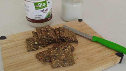Einige Scheiben Käckebrot mit Kürbiskernen und Sesam liegen auf einem Brett mit einem Buttermesser.