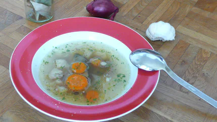 Ein Teller mit Suppe, in der Fettaugen, Rüben, Sellerie und Lorbeerblätter schwimmen.