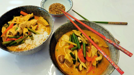 Zwei Schalen mit Hähnchen, Paprika, Bohnen und Bambussprossen in einer Sauce aus Curry und Kokos. In einer Schale ist zusätzlich Reis.