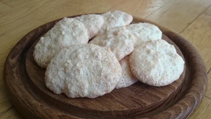 Zehn Kokosmakronen auf einem Holzbrett. Sie sehen fluffig aus.