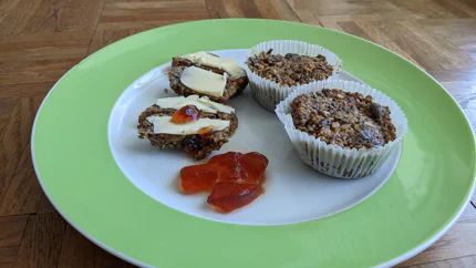 Vier Gebäcke aus verschiedenen Körnern und Nüssen in Muffinformen. Dazu gibt es Butter und Marmelade.