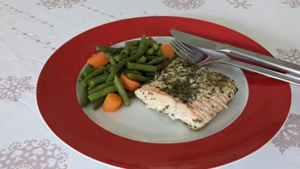 Ein Lachsfilet mit Kräutern, dazu gibt es grüne Bohnen und Karotten.