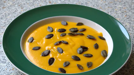 Ein Teller mit orange-gelber Kürbisscremesuppe. Darauf liegen geröstete Kürbiskerne.
