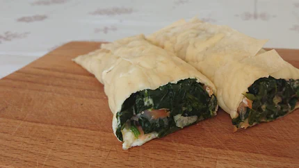 Eine halbierte Lachsrolle mit Filoteig und Spinat auf einem Holzbrett.