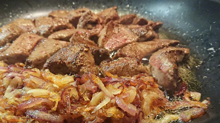 Leberstücke und angeschwitzte Zwiebeln werden in einer Pfanne angebraten.