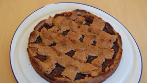 Eine Linzer Torte mit braunem Rand und ungleichmäßiger Verzierung aus Haselnussstreifen.