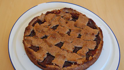 Eine Linzer Torte mit braunem Rand und ungleichmäßiger Verzierung aus Haselnussstreifen.