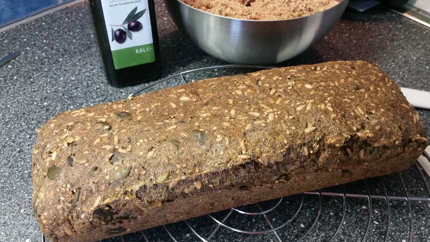 Ein Laib Brot auf einem Rost. Man sieht schon von außen, dass Kürbis- und Sonnenblumenkerne eingearbeitet wurden.