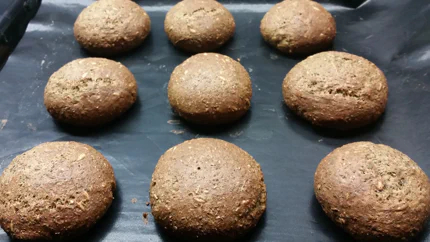 Neun kugelförmige, braune Brötchen auf einem Backblech.