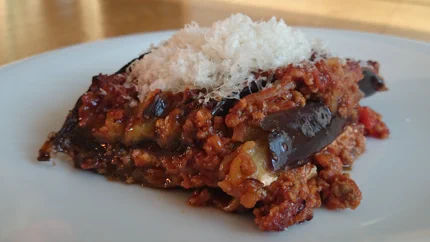 Eine Portion Moussaka auf einem Teller, das mit  geriebenem Parmesan abgeschmeckt wurde.