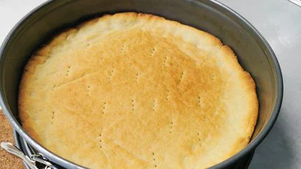 Ein goldbrauner Mürbteig in einer runden Form, in dem Pikser der Gabel zu sehen sind, damit der Teig nicht aufgeht.