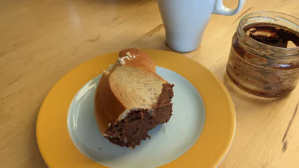 Eine zähflüssige Paste aus Haselnüssen, Schokolade und Kakao ist auf einem Stück Zopf verstrichen.