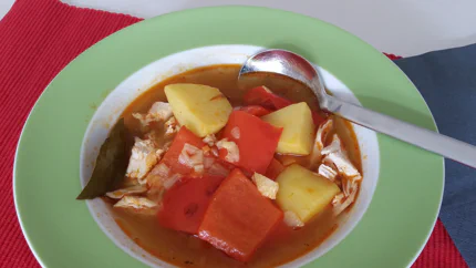 Stücke Paprika, Kartoffeln, Hühnerfleisch und Lorbeer schwimmen in einer roten Gulaschsuppe.