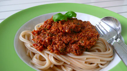 Satt rotes Pesto aus Tomaten und Parmesan auf einer Portion Spaghetti, garniert mit Basilikumblättern.