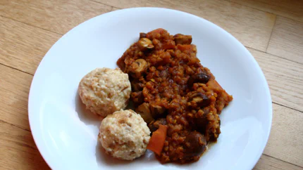Ein dickflüssiges Ragout aus Pilzen, roten Linsen und Karotten. Daneben liegen zwei Knödel auf dem Teller.